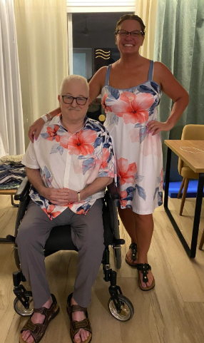 Ralph sitting in wheelchair and Kara is standing next to them. They are wearing matching outfits with flowers